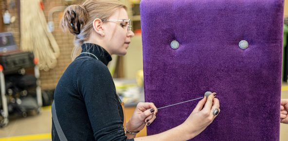 Photo d'une élève ajoutant un bouton sur le dossier mauve d'une chaise rembourrée